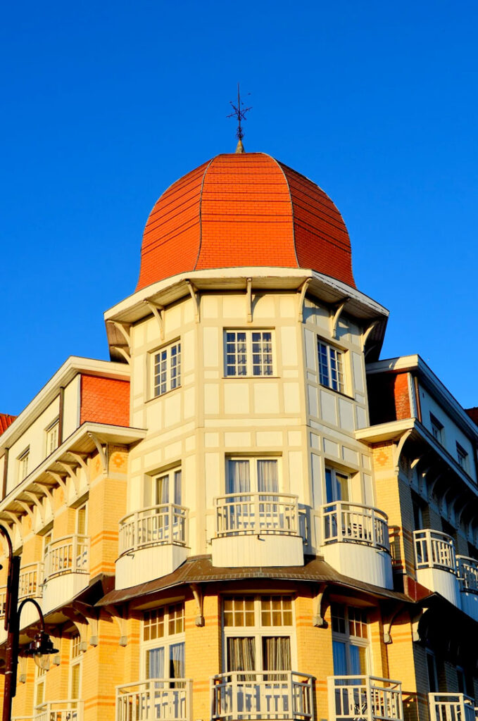 the french architecture influence in de hanne ann zee during golden hour adding an amber hue to the building. It's a tower, but rounded on three corners, and an edged domed orange roof. This is in perfect contrast to the perfectly clear and crisp blue sky behind it. 