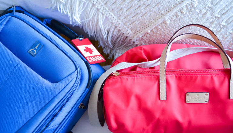 travel packer suitcase options. a blue travel pro carryon with a canada luggage tag with the maple leaf. And a bright red with beige accents Kate Spade duffel bag. There's a white knitted blanket behind them