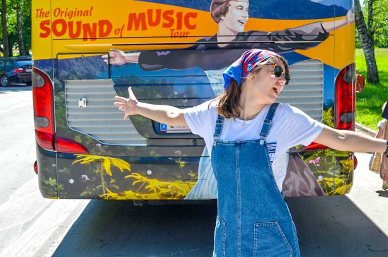 woman wearing overalls and bandana spreading arms in front of a bus with julie andrews from the sound of music in salzburg austria