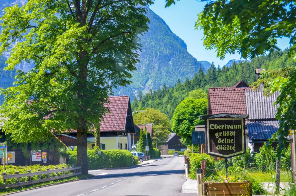 Sign welcoming you to the town of Obertraun with mountains in the background green trees lining the street