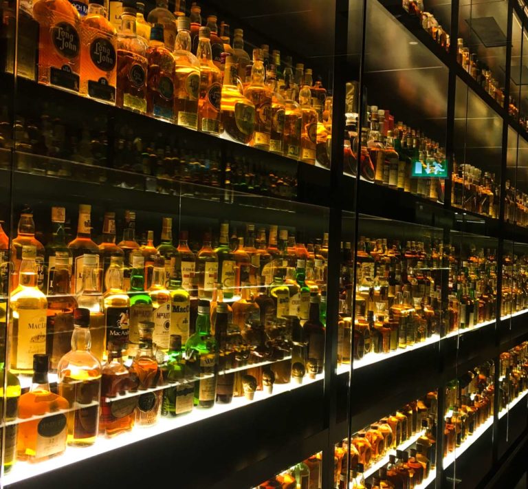 whiskey experience scotland Edinburgh attractions a giant wall of thousands of whiskey bottles, dimly lit for ambience behind glass doors