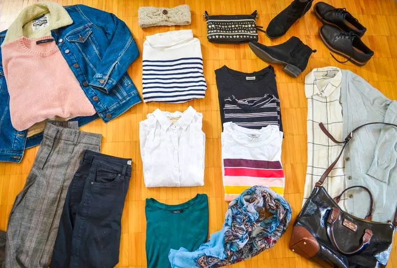 clothes nicely laid out on the floor, a Belgium packing list for fall travel in a carryon. 

From the left to right: a sherpa lined jean jacket, with a pink knit sweater laid inside. Below, are two pairs of pants, a plaid pair and black jeans. In a single column is a headband, a striped turtleneck, a short sleeve blouse, and a tshirt. Then there's a small purse, three graphic t shirts, and a scarf. On top there's a pair of leather oxfords, and a pair of black booties, below is a long sleeve blouse inside a cardigan with a large purse below