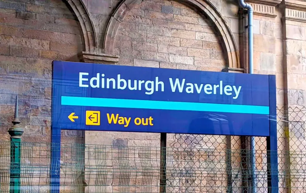 day trips from edinburgh by train waverly station the sign is in blue against the old stone wall of the station
