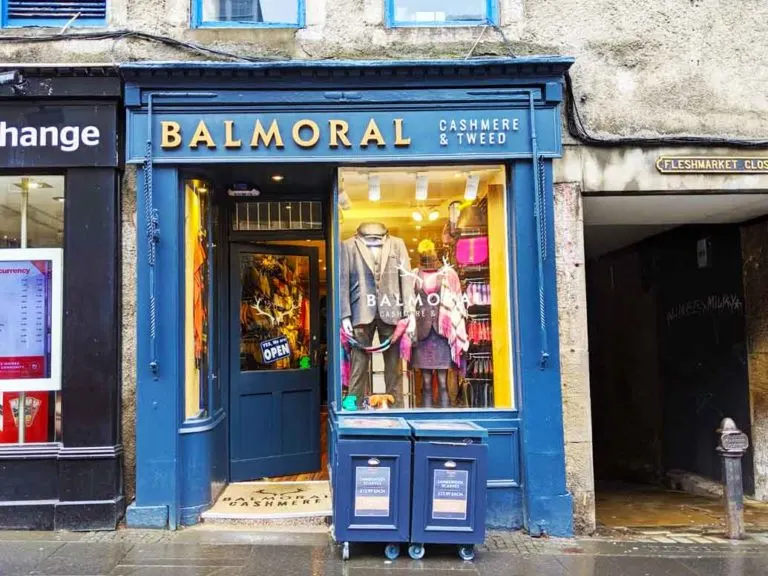 balmoral-tartan-scarf-scotland window front a blue paint with gold lettering for Balmoral you can see a man and a woman mannequin in the window sporting some tartan and tweed looks