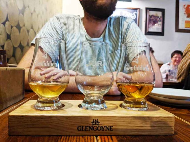 three glencairn glass souvenir filled with whisky in front of a man at a bar