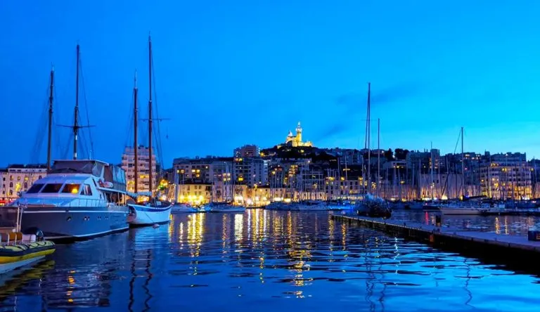 blue hour marseille old port views still water with boats and a lit up basilica in the backgorund on the mountain