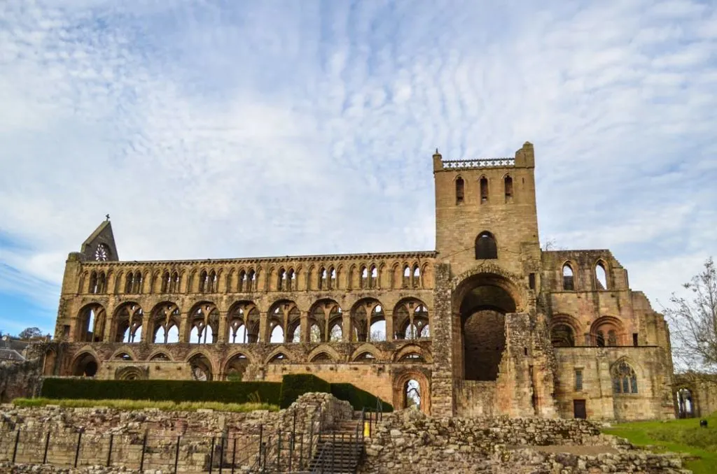 a ruined abbey sits atop a small hill. It's long and at least four stories tall, there isn't a roof, but the stone work is impeccable, with arch windows and grand doorways. There's a tower offset on the right side, adding even more height to this ruined abbey. 