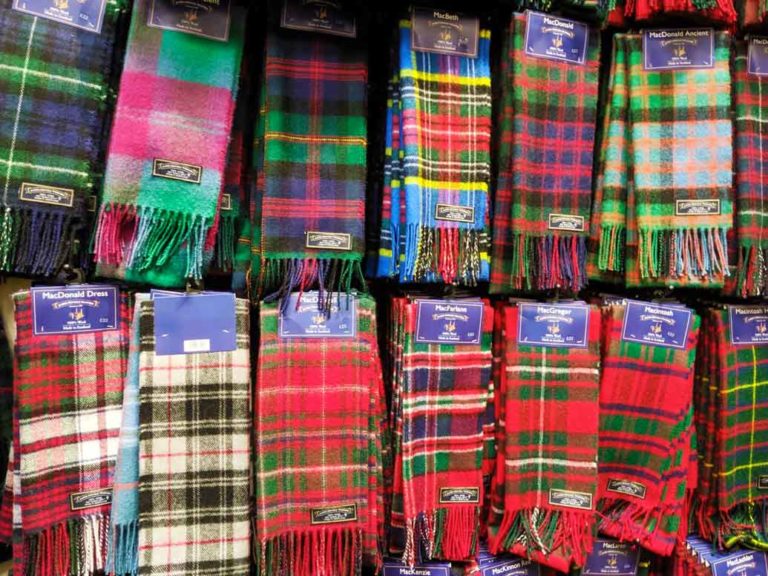 tartan-scarf-scotland-souvenir two levels of red green and blue combination of tartan scarves hanging on hooks in a shop.