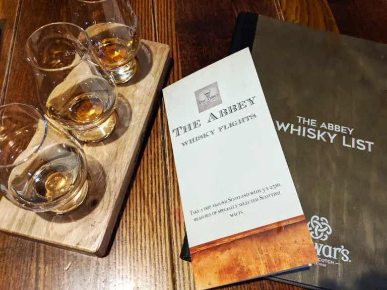 overhead picture: 3 glencarin glasses filled iwth whiskey, the abbey whiskey flights menu, and the abbey whiskey list menu