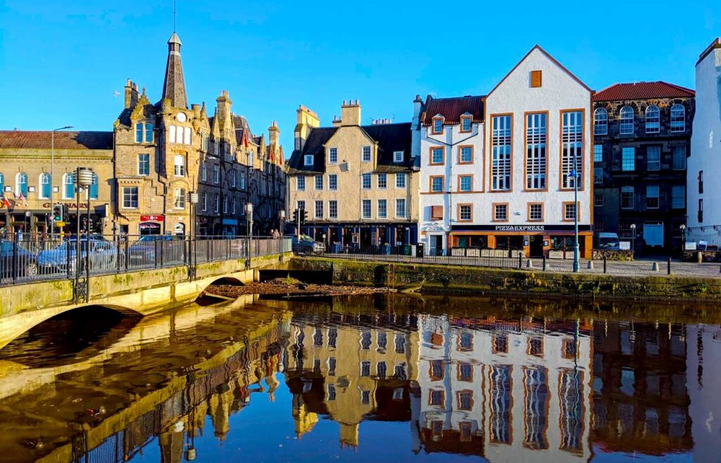 leith-edinburgh-scotland-reflections-on-the-water-of-the-biuldings-and-one-with-a-spire-with-a-bridge-leading-over-the-water