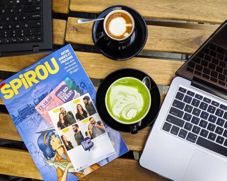 my-little-cup-cafes to work in brussels city centre. Overhead view of computers with espresso and matcha latte with Spirou comic book 