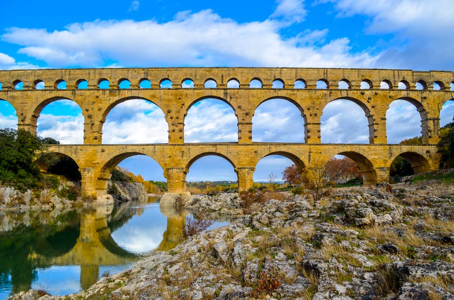 The epic pont du gard in the south of France. An ancient Roman aqueduct that's three levels of arches. The top level is where the water once flowed, with the smallest and the most archways. Below you have two levels of similar sized, larger archways. You can barely see the river flowing below, and you can make out a slight reflections, creating a fourth level of archways in the water. Most of the river is covered by the large rock pathway