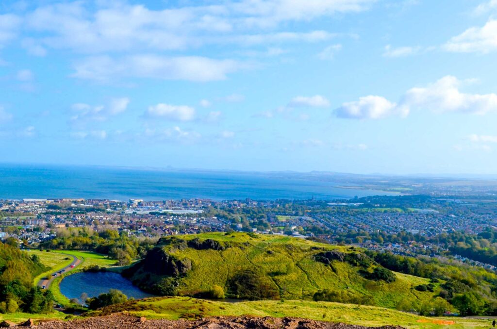 the-view-over-edinburgh-from-arthurs-seat-you-can-see-the-city-and-the-water-beyond-it-on-a-very-sunny-day-in-scotland