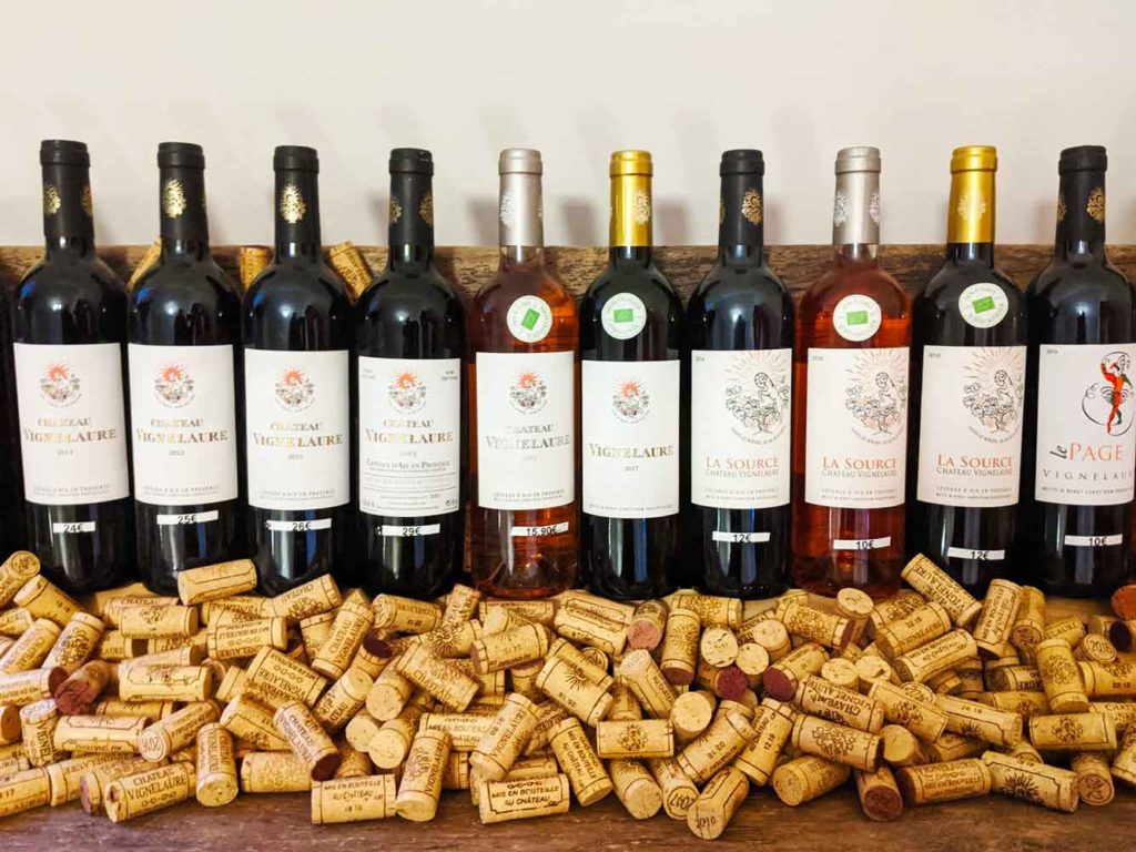 wine tasting in provence: 10 bottles of wine are lined up on the counter top. Thousands of used wine bottle corks sit in front of them. 