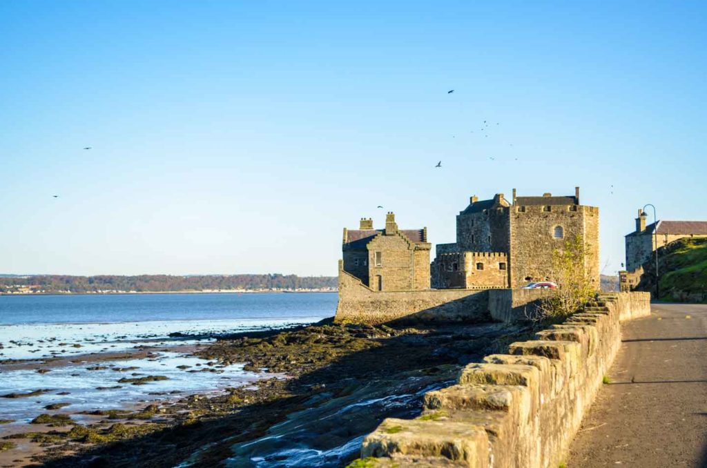 blackness castle stop edinburgh to st.andrews. A short knee high wall made of stone separates the sea from the road, it leads your eye straight to the stone castle in the distance. It looks more like a stone house than a castle, but there are four different sections to it. 