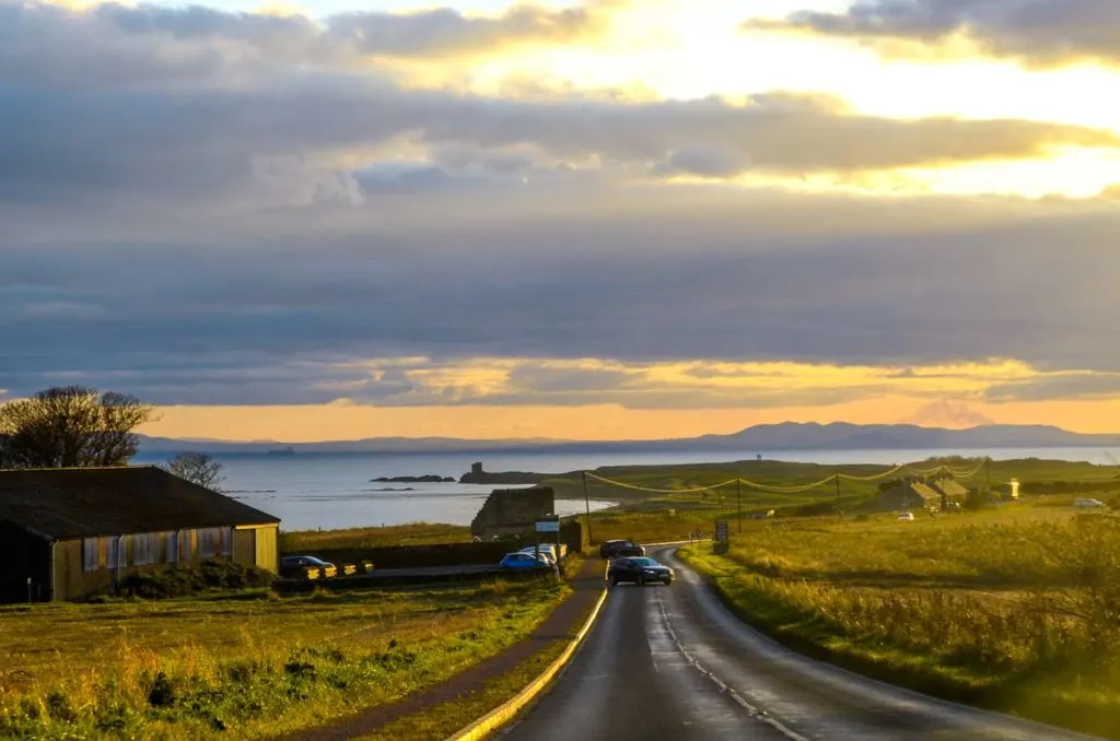 on the drive from Saint Andrews to Edinburgh trying to beat the setting sun. Although it makes for a stunning drive back. It's an overcast sky, but the setting sun is able to peak through, creating orange and blue stones above the water and fields on either side of the road. 