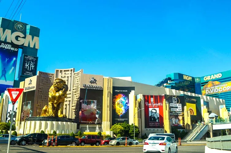 the end of the Las Vegas strip with the MGM Grand las Vegas hotel on the corner. There's a giant golden lion welcoming you (but also terrifying you!). Billboards line the side of the hotel. You see the hotel portion in the background at the top it says MGM GRAND. 
