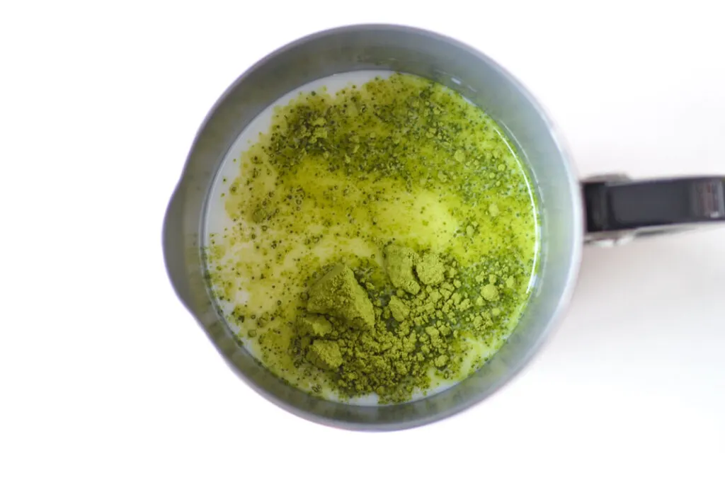 overhead view of a nespresso milk frother on a white table. There's milk inside with clumpy green matcha