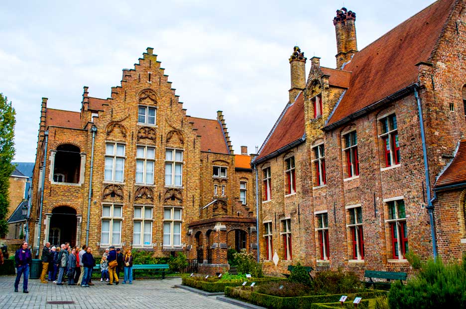 a group of people huddle next to old style brick buildings in europe. 