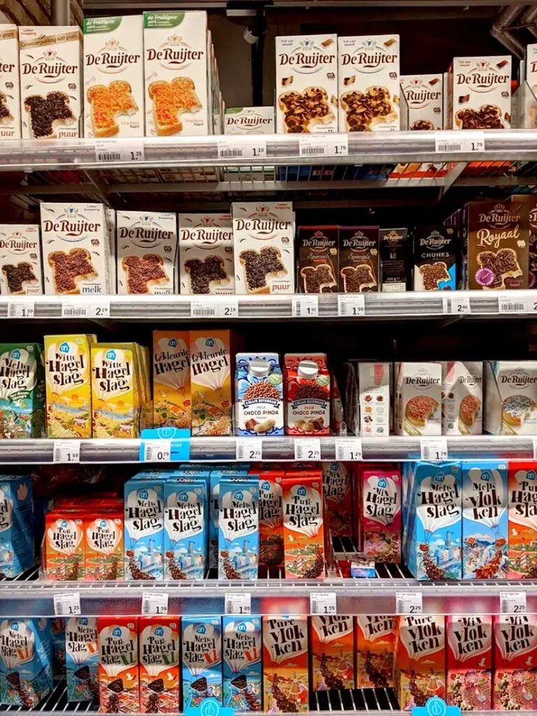 breakfast in amsterdam from the grocery store. There are five shelves filled with different types and brands of hagelslag - chocolate sprinkles. The top two shelves have de ruijter, and another brand is below