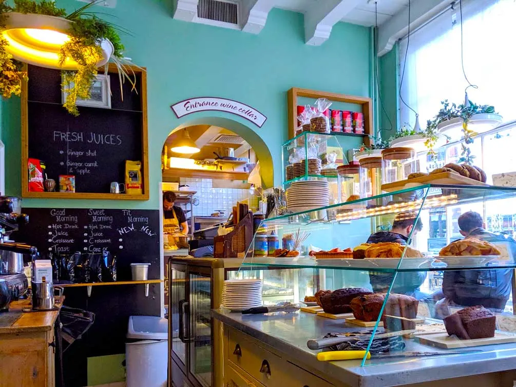 inside mellys cookiebar in amsterdam: a teal painted wall is filled with chalboards with the days meny and shelves selling theor products. You can see the counter with pastries galore from pies to cookies and loafs