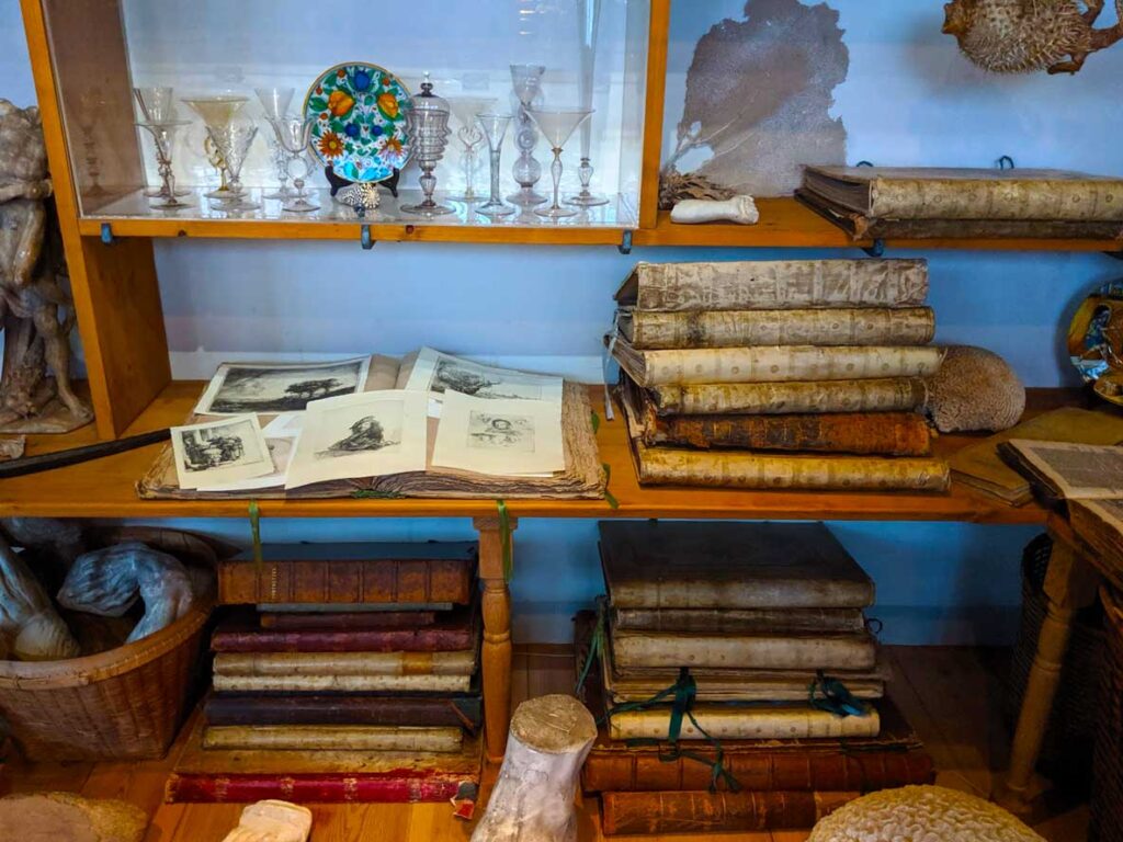 Rembrants house museum amsterdam a photo of three filled shelves in rembrandts studio.Old parchment books are closed and stacked, one is open and you can see some of his sketches. 