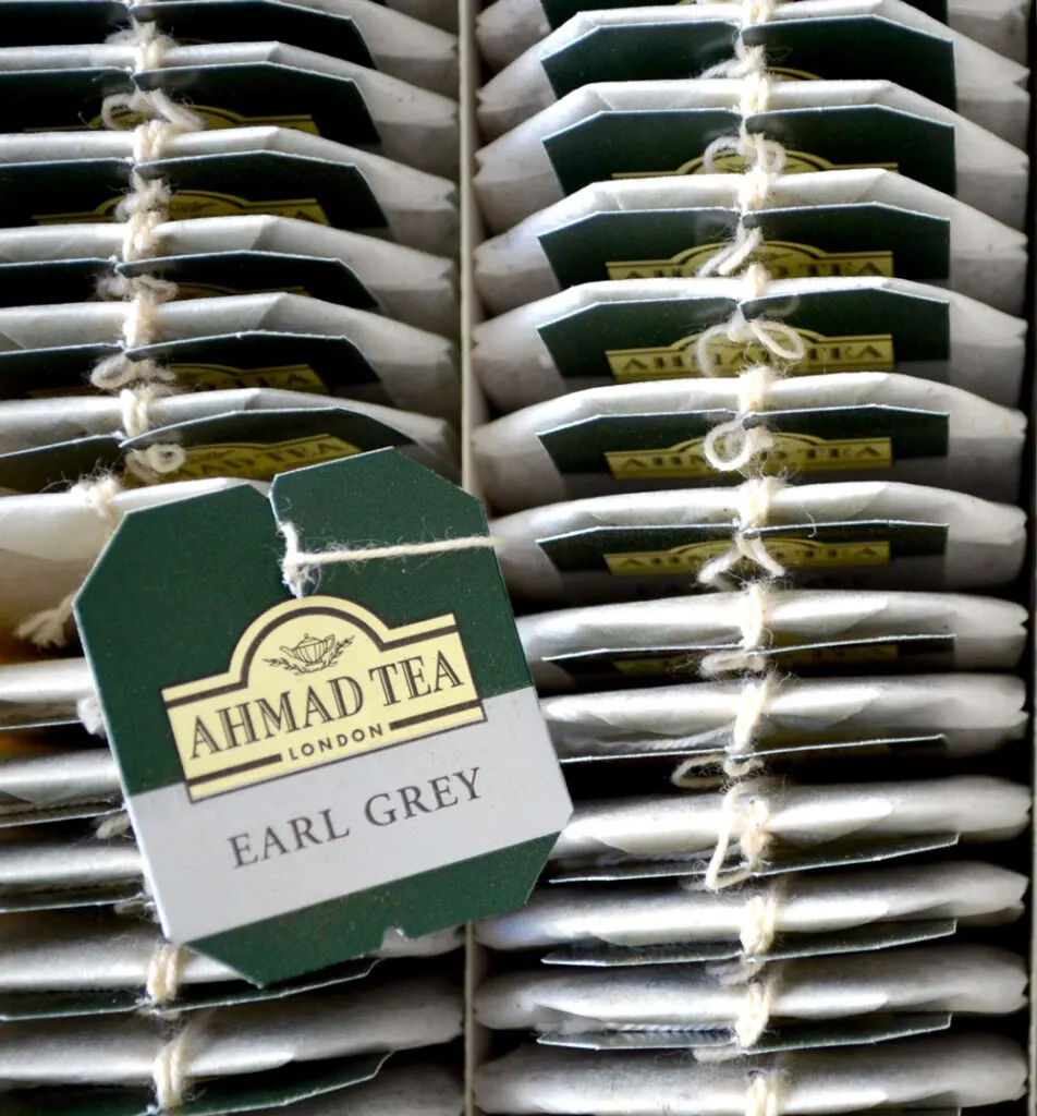 a topdown closeup view of a box filled with ahamd earl grey tea bags all in a single file row. There are two columns of these tea bags. Resting on top of them is a tea bag tea that has the ahmad tea logo and it says earl grey below.