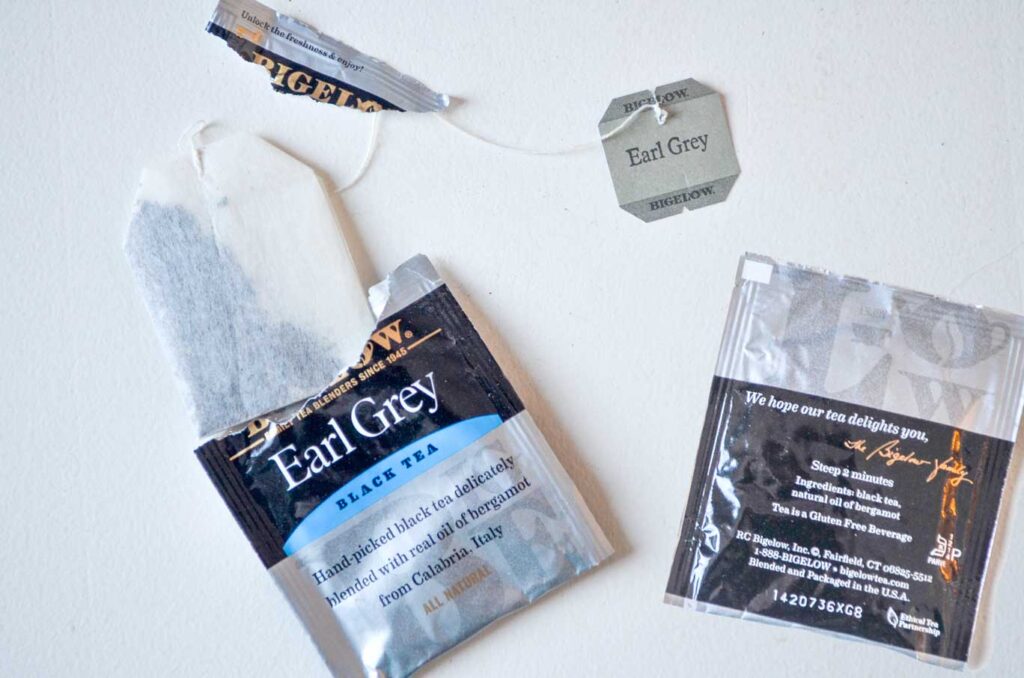 an overhead photo of two individual tea bag packages. The one on the left has been ripped open and the tea bag is starting to come out, the string going all the way into the middle before reaching the label for Earl grey tea. The second package is upside down. The packages are grey and black. There's a bit of blue on the front one where it says that it's a black tea. 