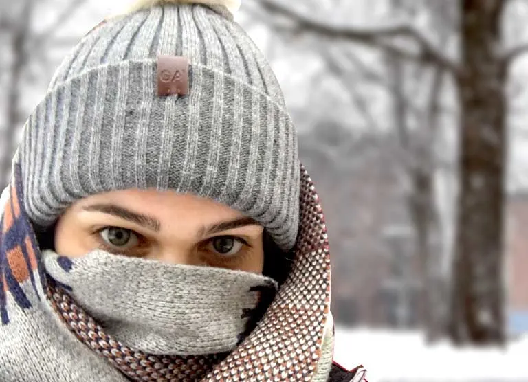 close up woman blundled in scarf and hat you can only see her eyes snow blurred background