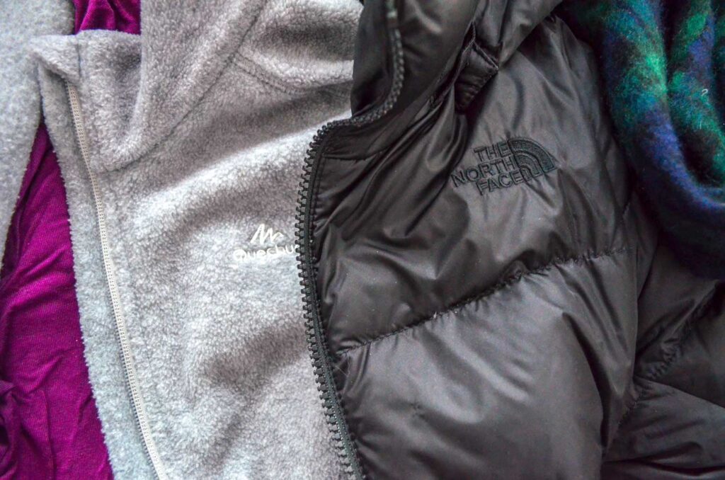 a closeup showing winter layers of clothing: a magenta turtleneck is on the bottom, a light grey polar fleece is next, and finally a black down-filled North Face jacket is on top.