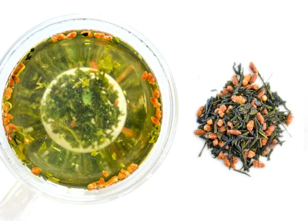 side by side comparison of the dry genmaicha Japanese tea leaf and the steeped tea in a doubled walled glass mug, and you can see the wet leaves on the bottom.
On the left is the steeped tea, it was steeped without a tea bag so the pieces of roasted brown rice are floating at the top, while the tea leaves have sunk to the bottom. The brew is a yellowish green colour. On the right is a pile of the dry leaves and rice.