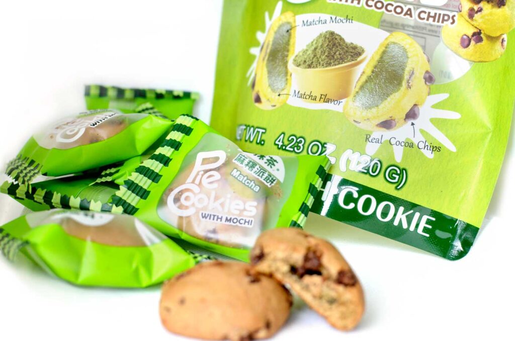 matcha chocolate chip cookie flavoured snacks. There are individually wrapped, with the larger package sitting behind. Two cookies have been unwrapped to showcase what they look like. They are rounded, taller than a typical chocolate cookie. The second cookie is bitten into to show the matcha filling, which you can barely see. 
