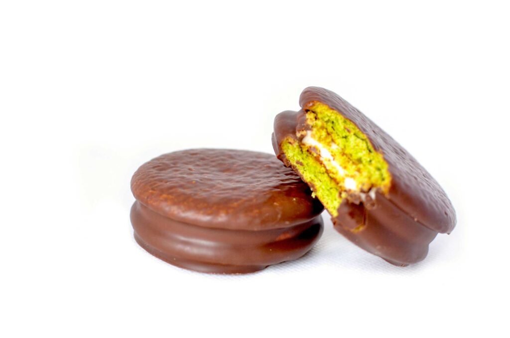 two choco pie on a completely white background. One is closed and ready to be tasted while the other is resting on top and has a bite taken out of it to showcase the green inside with a white creamy centre. 