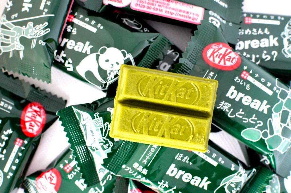 matcha flavoured kit kat snacks to try. Several individual wrapped dark matcha kit kat bars in dark green wrapping sit on a table. Each wrapping is different, there's a panda on one, a reindeer on another... One was opened and there's a mini green kit kat bar sitting on top of them all. 