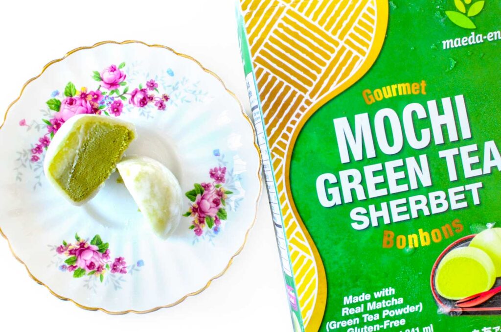 matcha green tea flavoured sherbert mochi. A packaging is on the right side, there's a nice floral plate on the left, with a cut open frozen mochia. The outside is white while the inside looks like a green tea ice cream filling. 