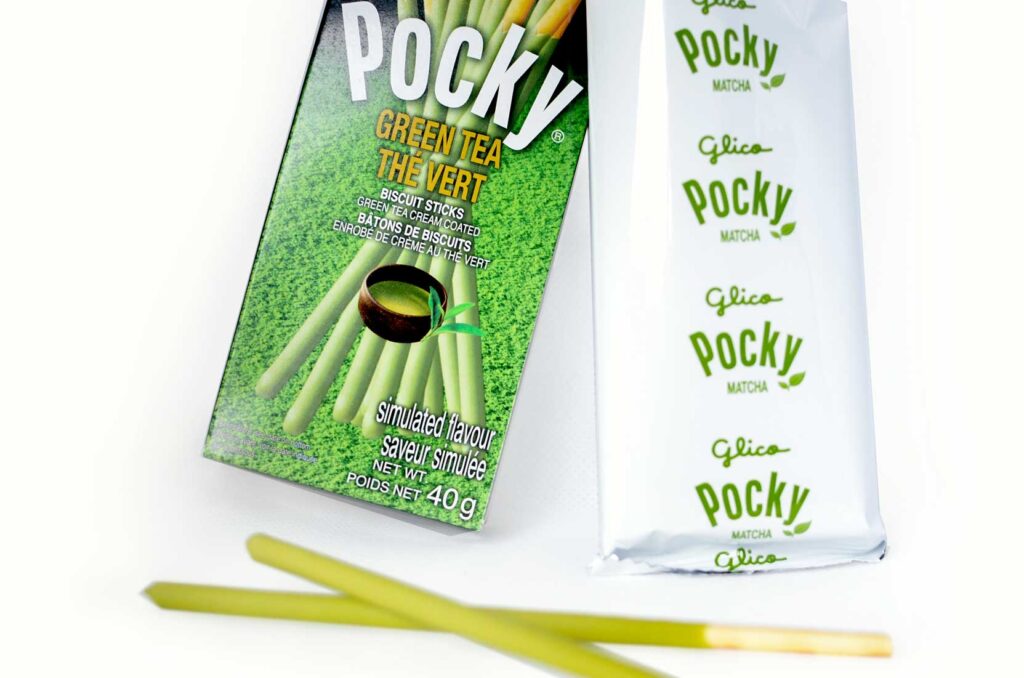 matcha green tea pocky snacks. A closeup of the box and the original packing on the inside that says Glico Pocky in green. There are two examples of the preztel sticks that are now covered in green instead of the regular chocolate. 