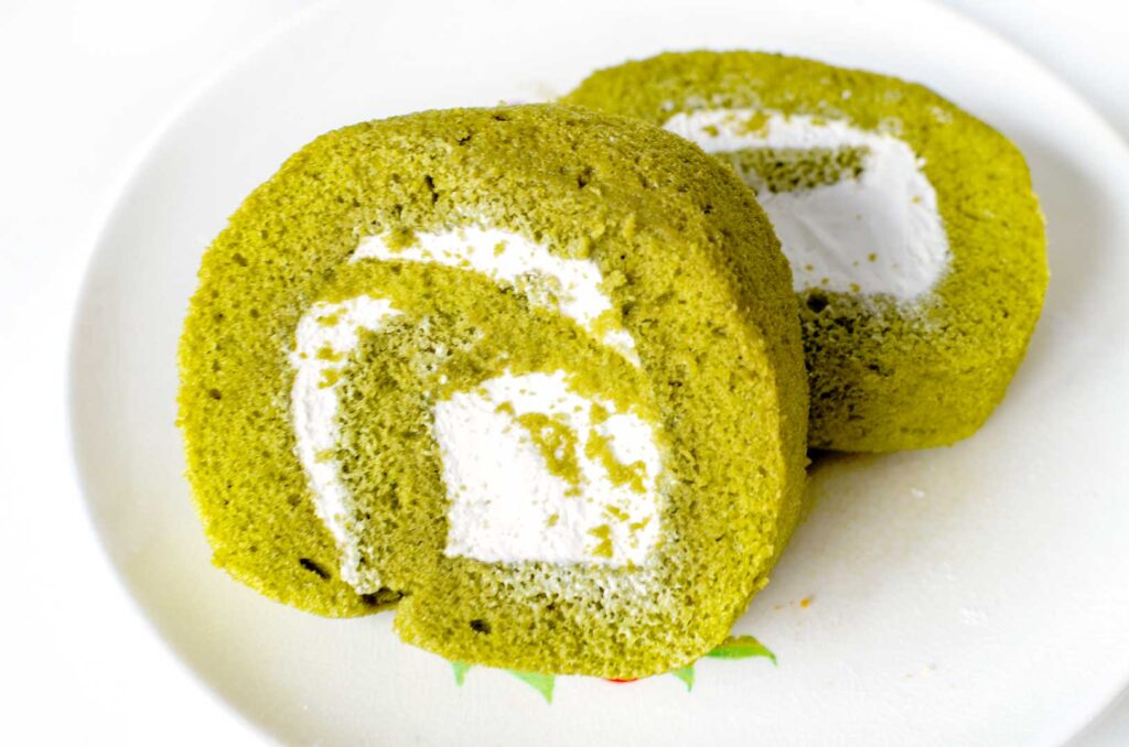 two pieces of matcha cake on a plate. They are spiral roll cakes. The cake itself is green, you can see the spiral made from white creamy centre. 