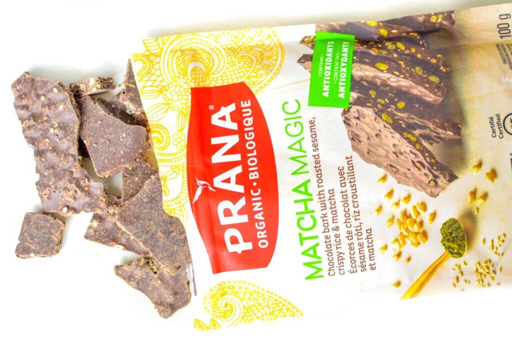 prana matcha magic green tea flavoured snack is on a table and spilling out of the packaging. It's dark chocolate chunks you can see bits and pieces inside the chocolate. 
