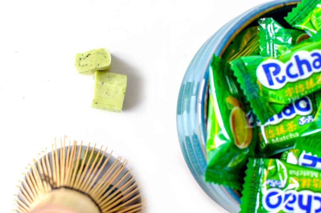 puchao matcha wrapped candy in a traditional matcha bowl. There are two unwrapped puchao chewy candy, they are light green with dark spots inside. 