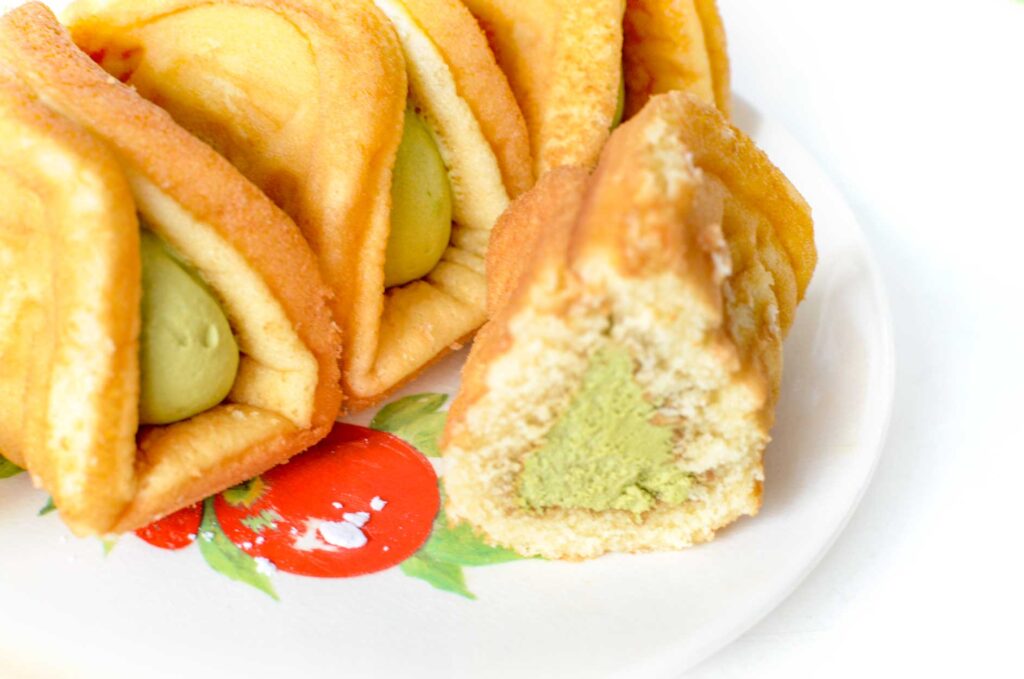 waffle matcha roll snack review. Four a fluffy pastries sit on a plate. They are pinched at the top to create a triangle around a creamy green filling inside. Three pastries sit untouched in the back, whilte the one in the front was cut in half to show more of the inside. 