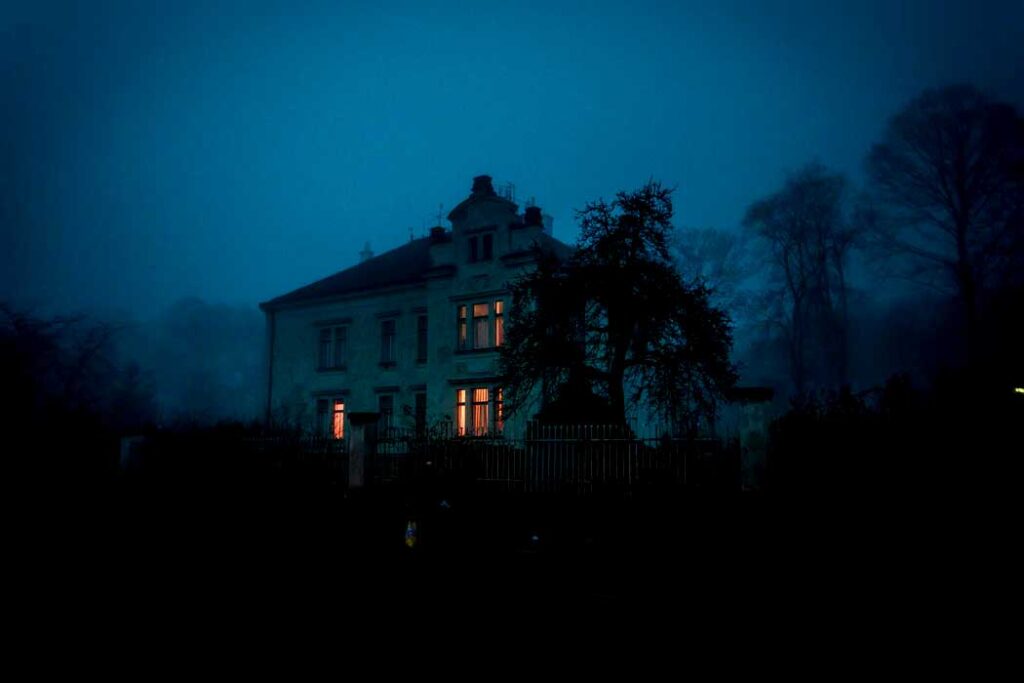 Photo by Ján Jakub Naništa on Unsplash.com

A spooky creepy dark scene of a haunted house. The grass and lawn is pitch black ,there's an outline of a tree next to the house. IT's a white mansion, some of the lights are on adding a yellow colour to the blue and black image. The sky is clear but a blue ambiance. It's kind of foggy evening as well as there are outlines of trees behind the house but they're lighter. 