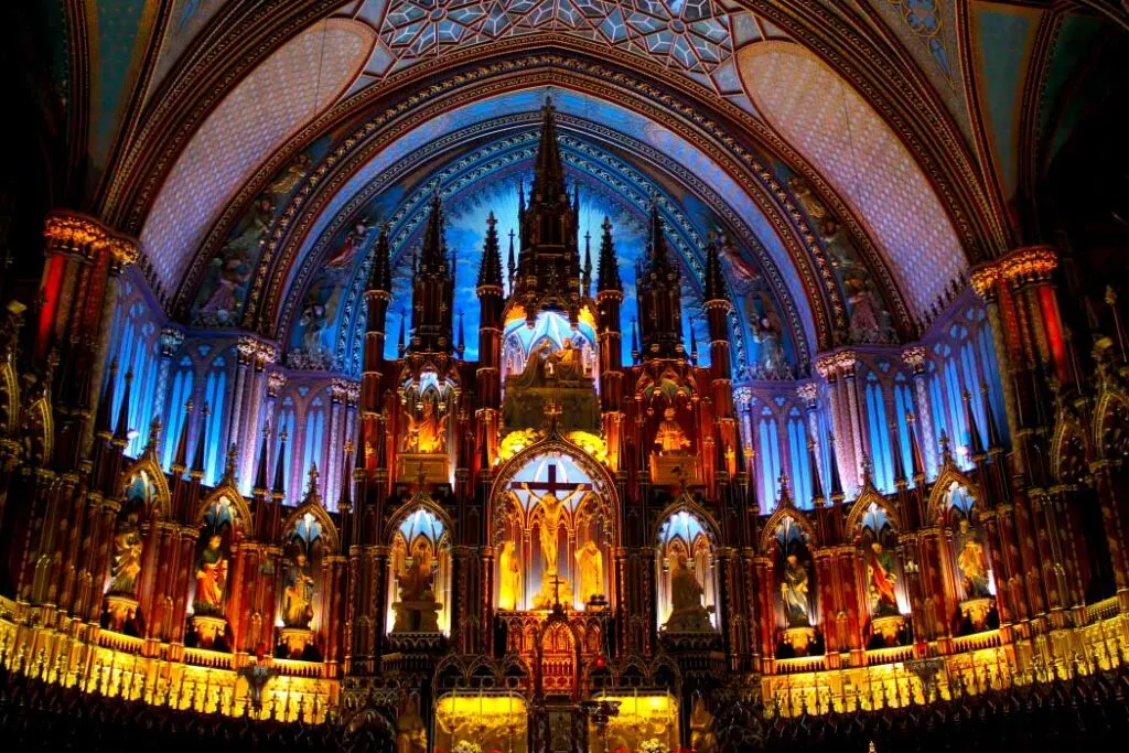 Photo by Kris Schulze on Pexels.com of the inside of the notre dame basilica candlelight on halloween in montreal. This is a photograph of the jaw dropping organ all lit up leading all the way up to the tall ceilings in the basilica. The lights are an orange, yellow, and blue tones. 