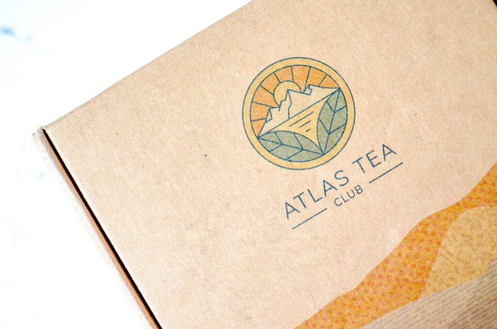 atlas tea club tea subscription box. A close up of the box before it's opened, I wonder what's inside!?

It's a very simple box with the logo and name Atlas Tea Club on it, very simple. The logo is a circle with a setting sun behind a mountain and a lake. On the bottom of the lake are two large tea leaves. 