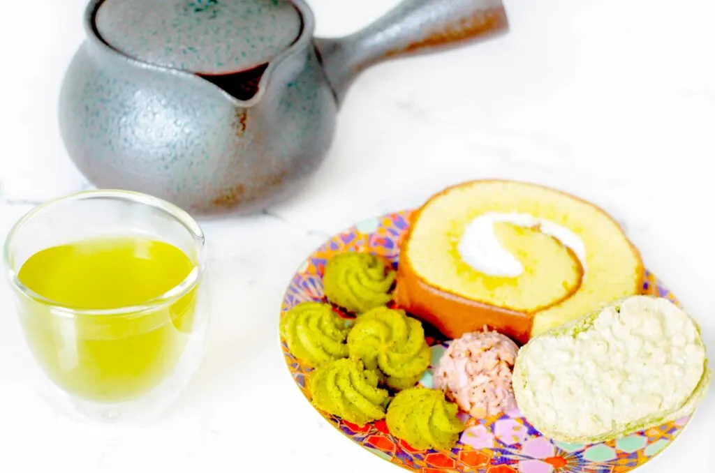 japanese snack plate from sakuraco subscription box with a double walled mini glass with a green brew inside. In the back is a traditional Japanese teal kyusu teapot keeping the rest of the tea warm
