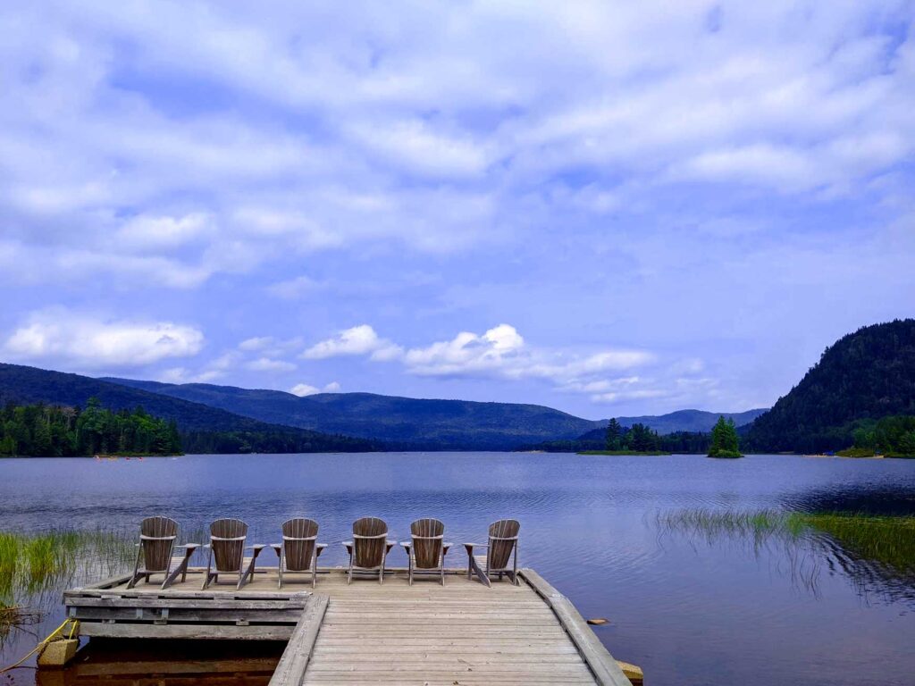 mont tremblant national park from saint sauveur summer. A large wooden dock with 6 chairs at the end, leads you out into the lake  with a relaxing view of the mountains in the distance. 