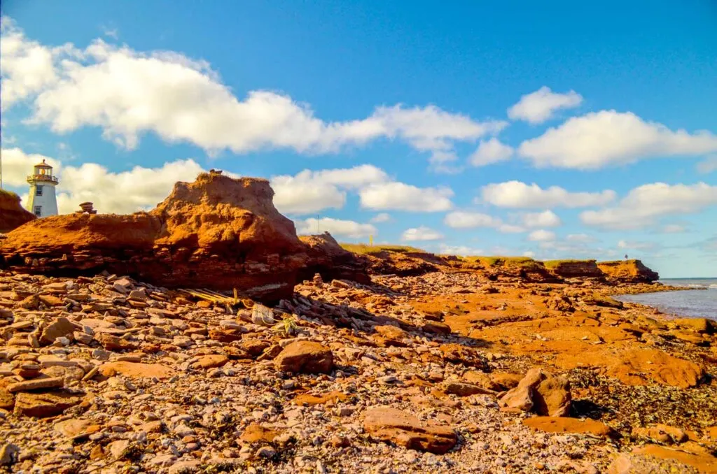 Trying to hide the telecommunications tower and wind energy plant in the photo by cropping the frame to include the incredible red rocks of prince edward island during low tide. Popping out behind the rocks, you can see a white and red lighthouse. 