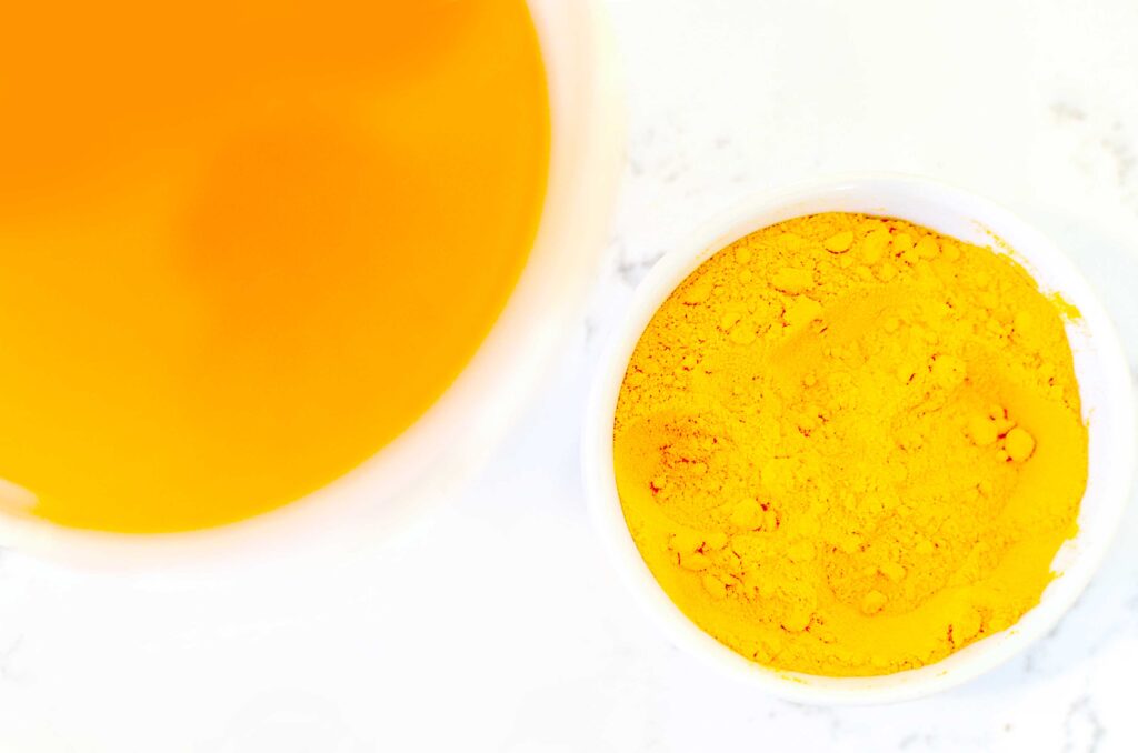 an overhead photo showing two circular kitchen ware items: a mug, and a pinch bowl. The mug has a deep orange brew, but inside the punch bowl is a heap of slightly lighter orange turmeric powder