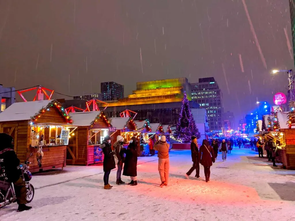 people enjoying the montreal christmas village booths while it's snowing