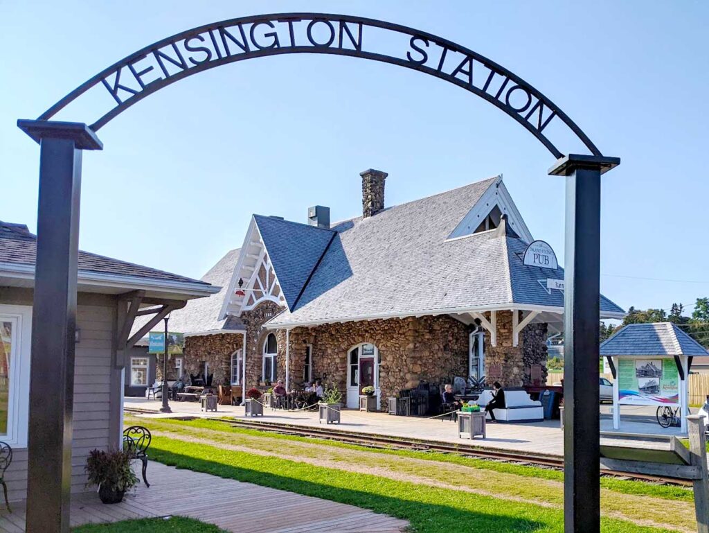 pei kensington train station. A large black iron archway welcomes you to the train station in Kensington. In the middle of the arch, it reads Kensington Station. Behind the arch, in the middle,  are the old railway track and where the train station used to be - a beautiful stone building. Now you can see a sign for the pub. 