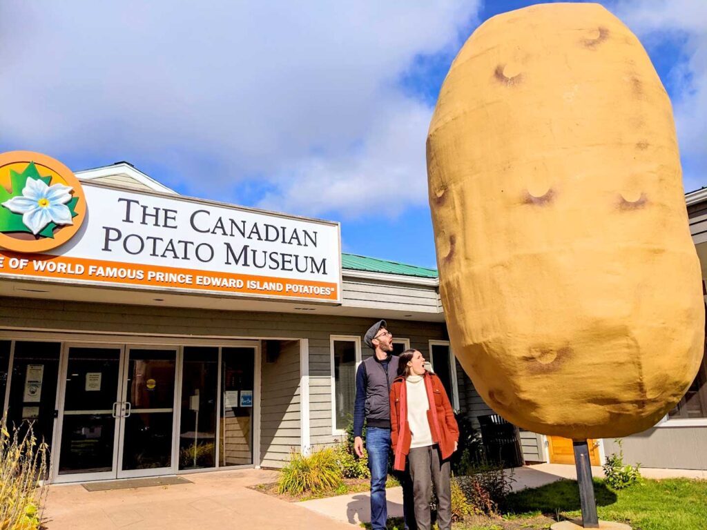 a one story building with a large sign: The Canadian Potato museum. In front is a couple looking in complete awe at a giant potato almost three times their hight and more than twice their width... combined!